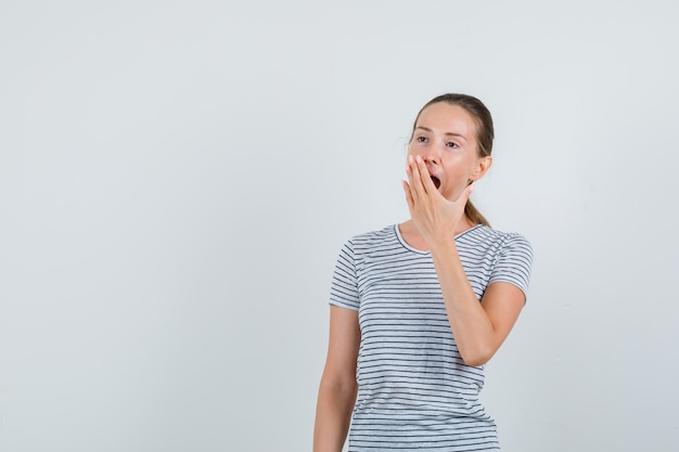 Tシャツであくびをして眠そうな若い女性。正面図。