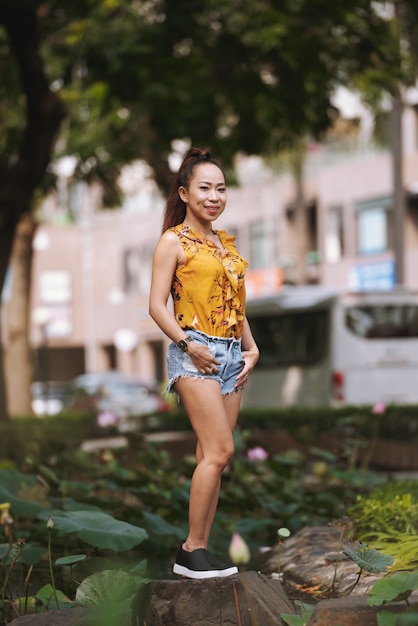 Young fit fashionably dressed Asian woman in shorts and bright blouse posing in urban street