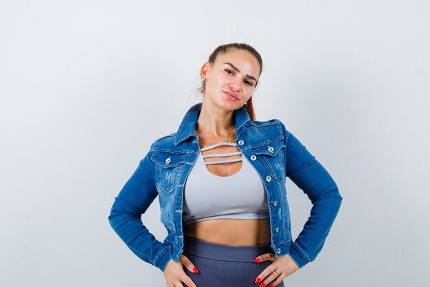 Young fit female in top, denim jacket posing while standing and looking pensive , front view.