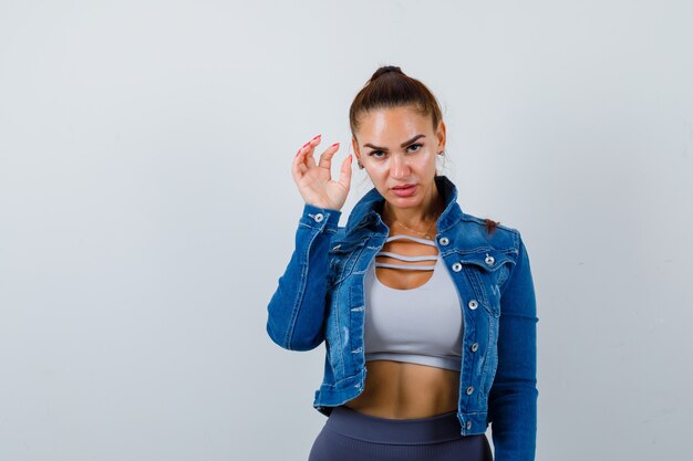 Young fit female in top, denim jacket showing claw imitating cat and looking aggressive , front view.