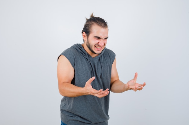 Young fit male keeping hands in aggressive manner in sleeveless hoodie 
 and looking angry. front view.