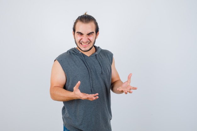 Young fit male keeping hands in aggressive manner in sleeveless hoodie  and looking anxious. front view.