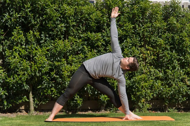 Young fit male practicing yoga and doing the triangle pose outdoors