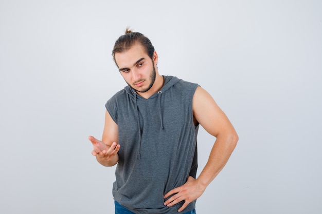Young fit male in sleeveless hoodie  streching hand towards camera and looking pensive , front view.