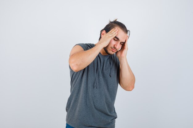 Young fit male in sleeveless hoodie 
 suffering from headache and looking unwell , front view.