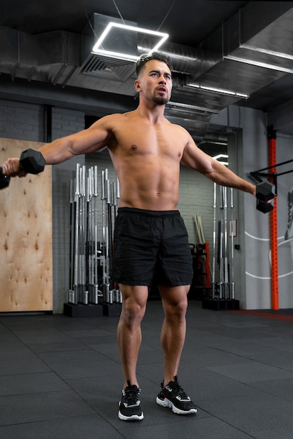 Young fit man working out with dumbbells at the gym