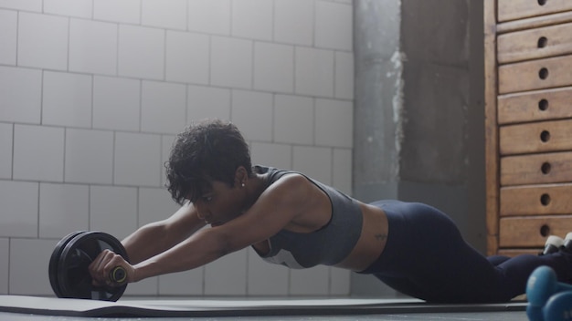 Free photo young fit and tone up mixed race woman doing fitness workout with abs wheel at loft during sunny day