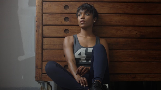 Young fit and tone up woman sits lean on wooden wardrobe during workout rest in loft