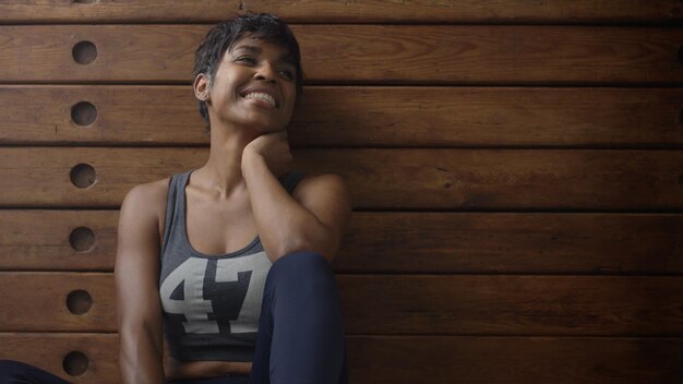 Young fit and tone up woman sits lean on wooden wardrobe during workout rest in loft