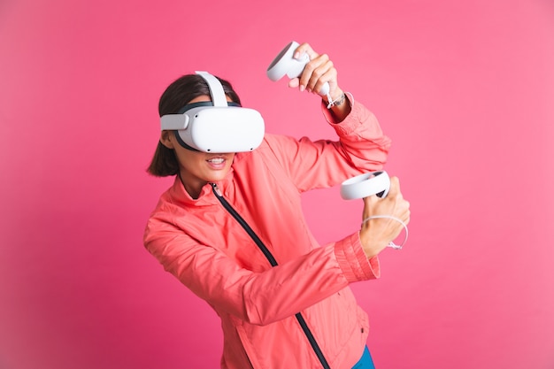 Free photo young fit woman in sport wear jacket and virtual reality glasses playing boxing fight games on pink