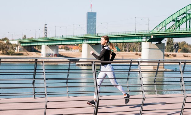 Молодая здоровая женщина в спортивной одежде, бегущая возле идиллической реки