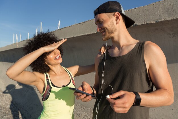Young fitness couple listening to music with earphones outdoors
