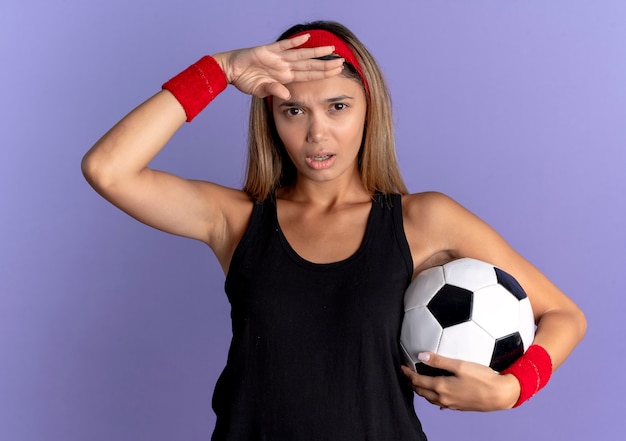 黒のスポーツウェアと赤のヘッドバンドでサッカーボールを保持している若いフィットネスの女の子