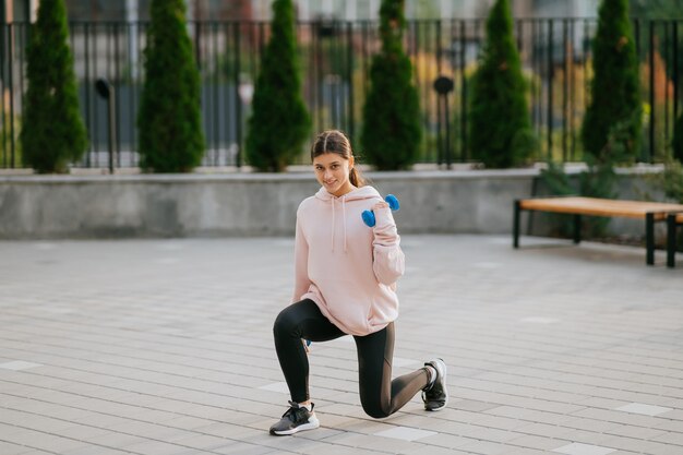 Young fitness girl making exercises with dumbbells in city park