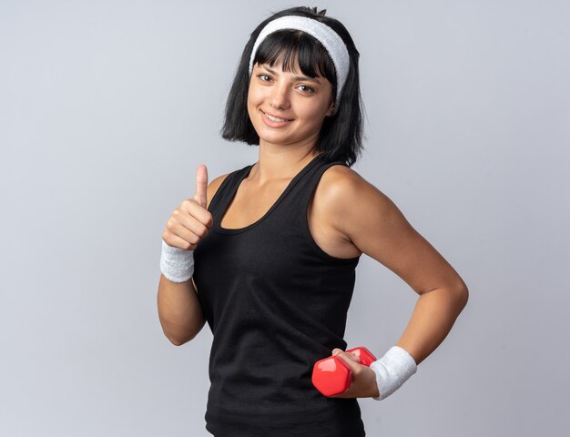 Young fitness girl wearing headband holding dumbbells doing exercises looking confident smiling