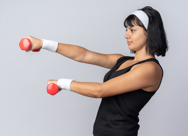 Free photo young fitness girl wearing headband holding dumbbells doing exercises looking confident standing over white background