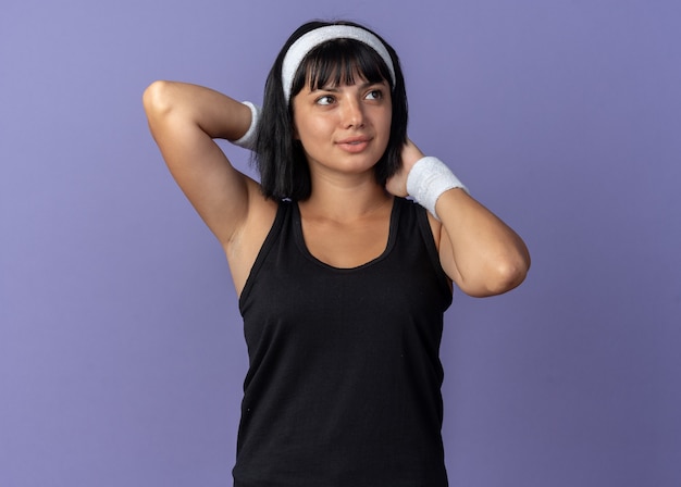 Бесплатное фото Молодая фитнес-девушка с повязкой на голову, протягивающая руки, уверенно выглядящая, стоя над синим