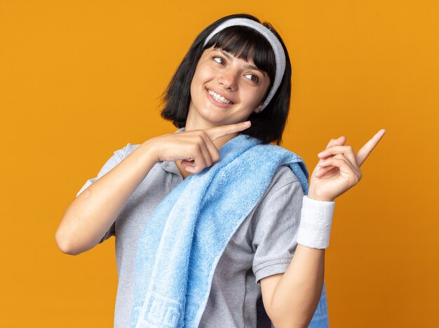 Young fitness girl wearing headband with towel on her shoulder looking aside happy