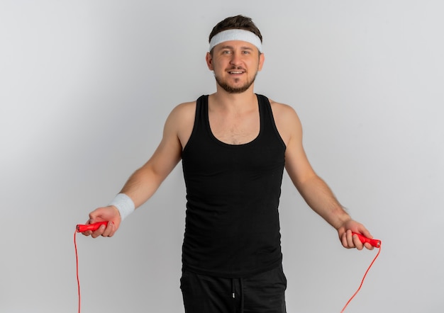 Young fitness man with headband jumping using skipping rope with happy face standing over white background