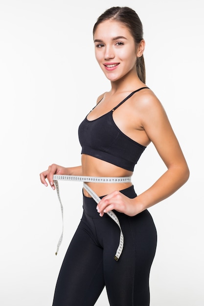 Young fitness woman measure with tape her belly isolated on white wall