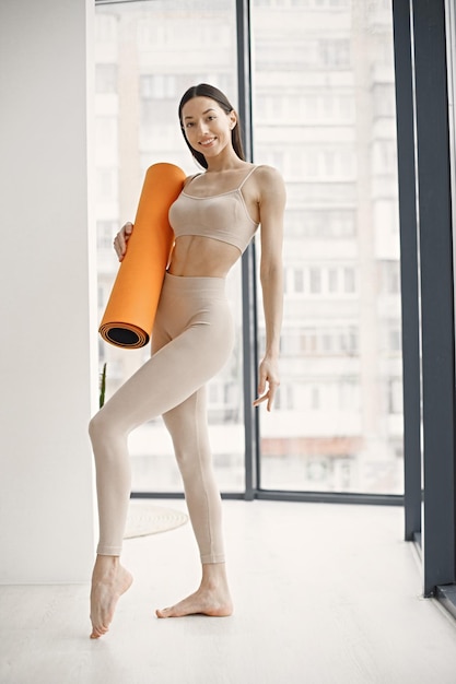 オレンジ色のヨガマットを保持しているトレーニングの準備ができている若いフィットネス女性