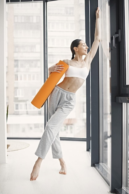 Giovane donna di forma fisica pronta per l'allenamento che tiene una stuoia di yoga arancione