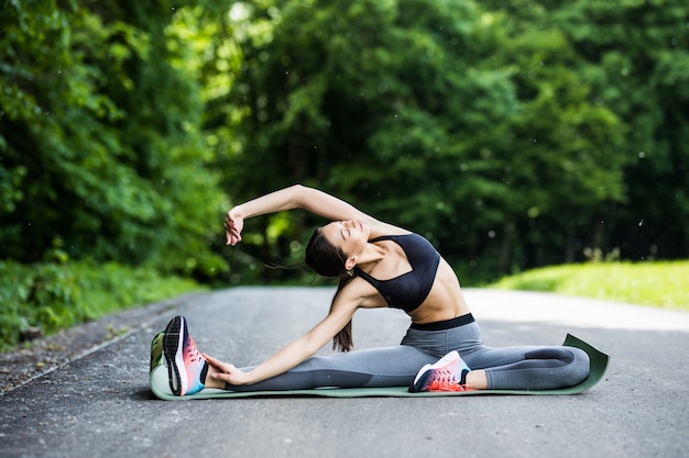 Young fitness woman runner stretching legs before run in the city park