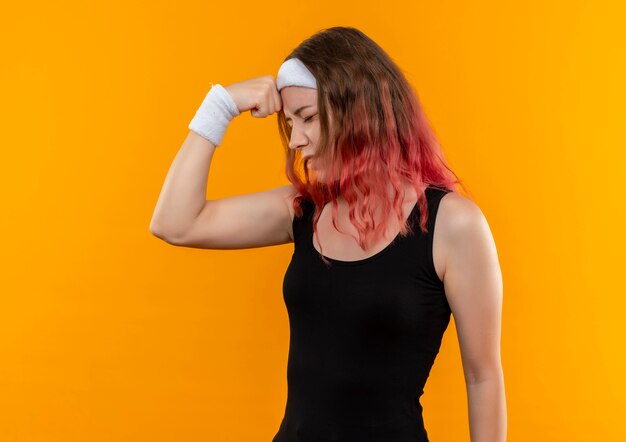 Young fitness woman in sportswear looking confused touching head for mistake