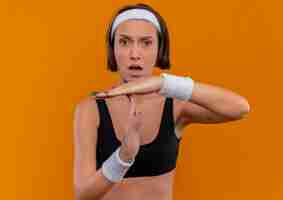 Free photo young fitness woman in sportswear with headband making time out gesture looking confused standing over orange wall