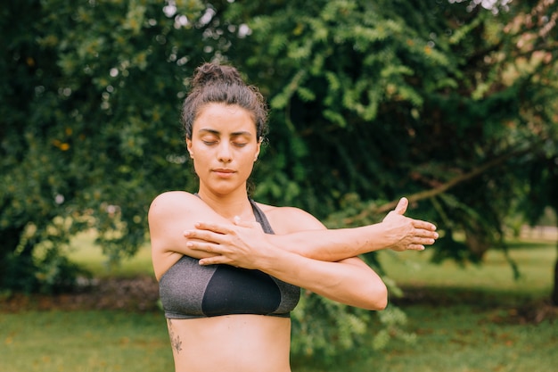 Young fitness woman with closed eyes stretching her hands in the park