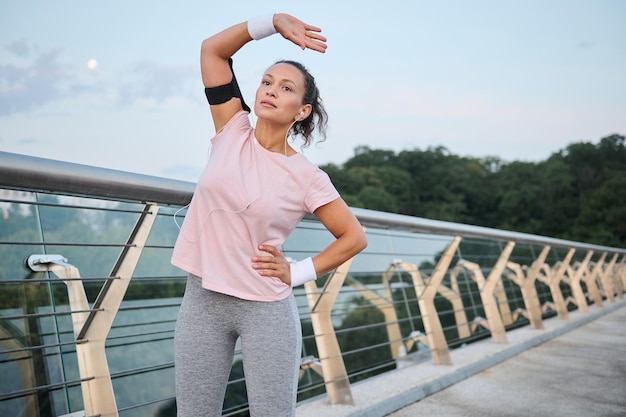 Young fitness woman working out outdoors on the bridge. sports women in sportswear stretching her body in the early morning at sunrise on the river coast. sports, motivation, healthy lifestyle concept
