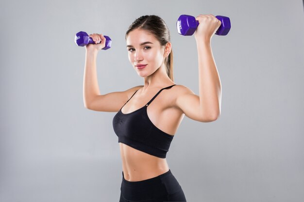 Young fitness woman working out with dumbbell isolated white wall