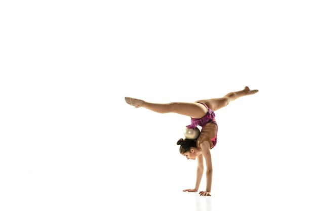 Молодая гибкая девушка изолированная на белой стене. Девушка-модель в качестве артистки художественной гимнастики занимается с оборудованием. Упражнения на гибкость, баланс. Изящество в движении, спорте.