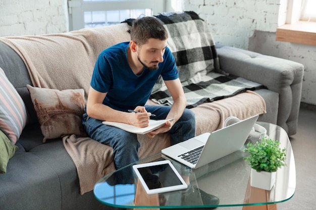Foto gratuita giovane uomo concentrato che studia a casa durante i corsi online o informazioni gratuite da solo