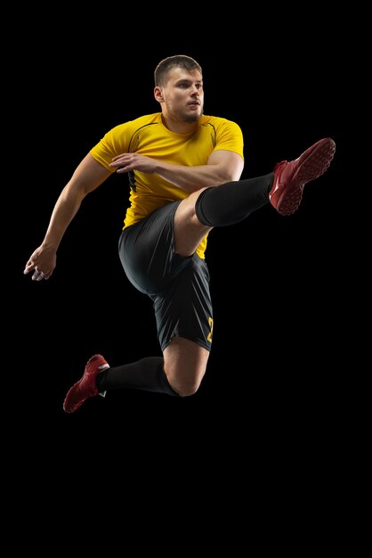 Young football soccer player training isolated on black wall