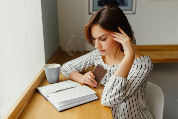 Young freelance girl worker sitting at cafe shop with phone, note book