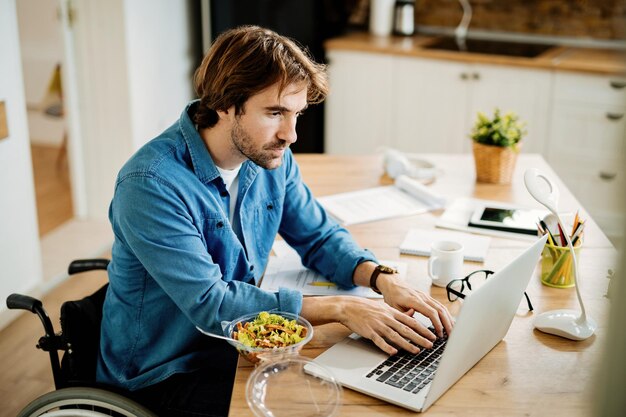 Young freelance worker in wheelchair working on a computer at home