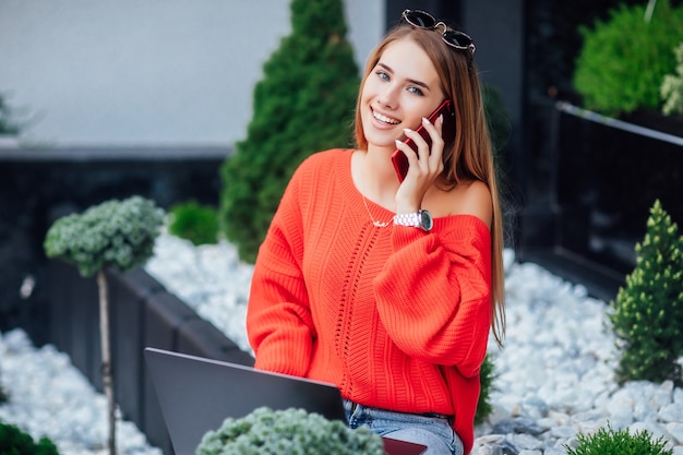 Giovane libero professionista, donna bionda di successo in camicia rossa con laptop che riposa fuori.