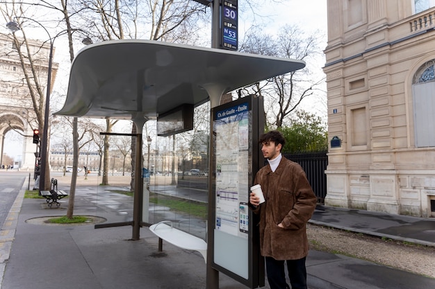 Young french man waiting at the station for the bus and drinking coffee