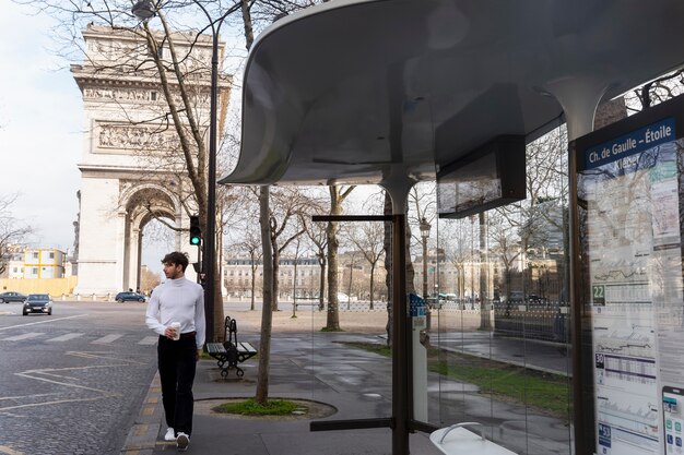 Young french man waiting at the station for the bus and drinking coffee