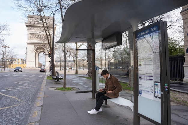 Молодой француз ждет на вокзале автобус и пользуется своим смартфоном