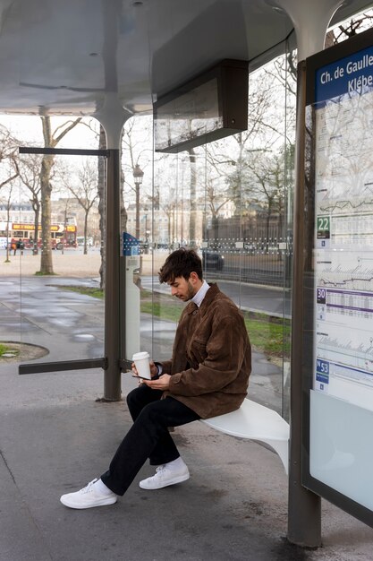 Young french man waiting at the station for the bus and using his smartphone