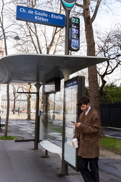 Young french man waiting at the station for the bus and using his smartphone