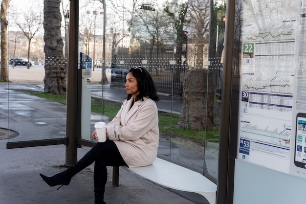 Foto gratuita giovane donna francese che aspetta alla stazione l'autobus e beve caffè