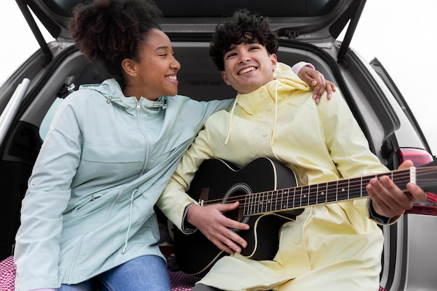 Free photo young friends playing the guitar on a familiar car trip