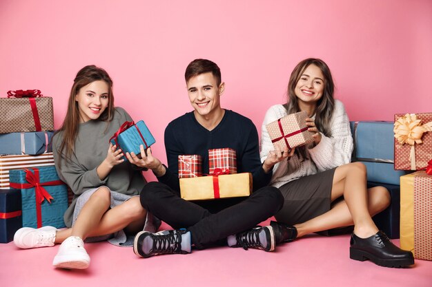 Young friends sitting among christmas gift boxes on pink