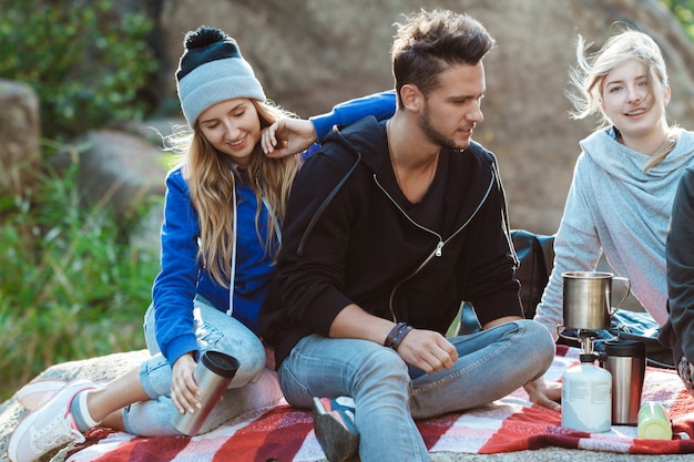 Young friends sitting on rock in canyon, smiling, drinking tea