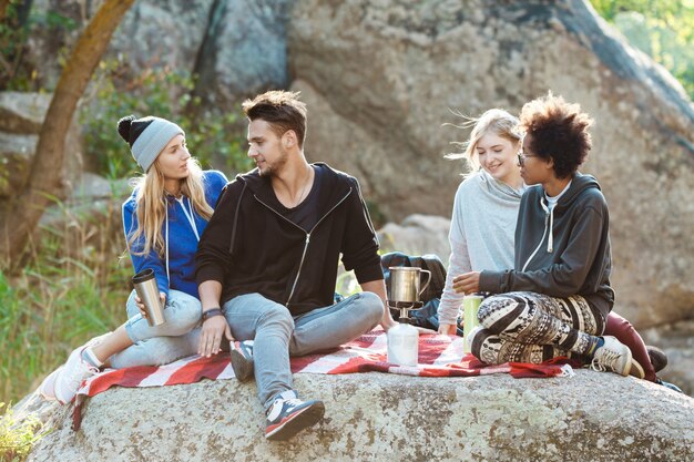 Young friends sitting on rock in canyon, smiling, drinking tea