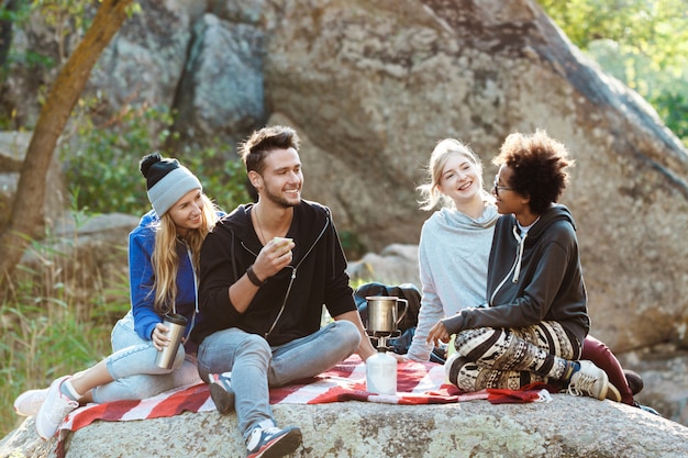 Young friends sitting on rock in canyon, smiling, drinking tea