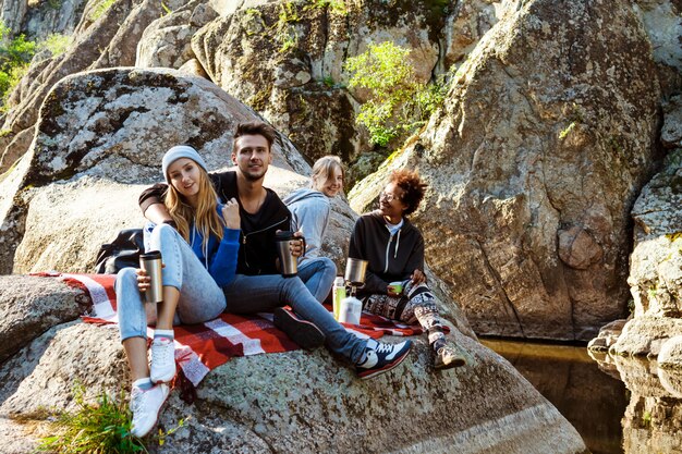 Young friends sitting on rock in canyon, smiling, drinking tea